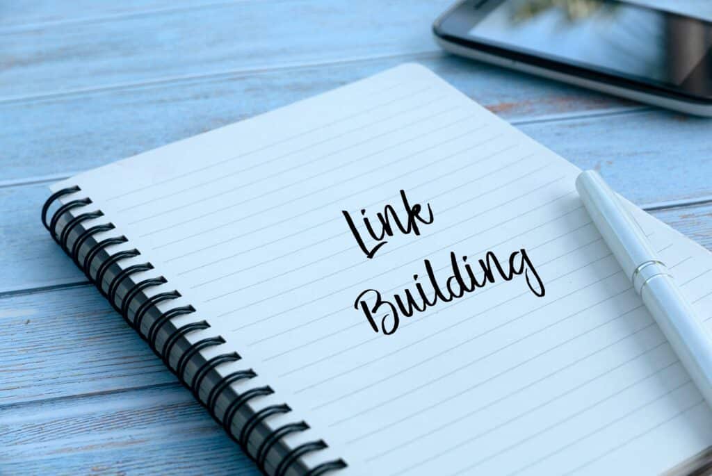 The words "Link Building" are written in a notebook that sits on a desk.