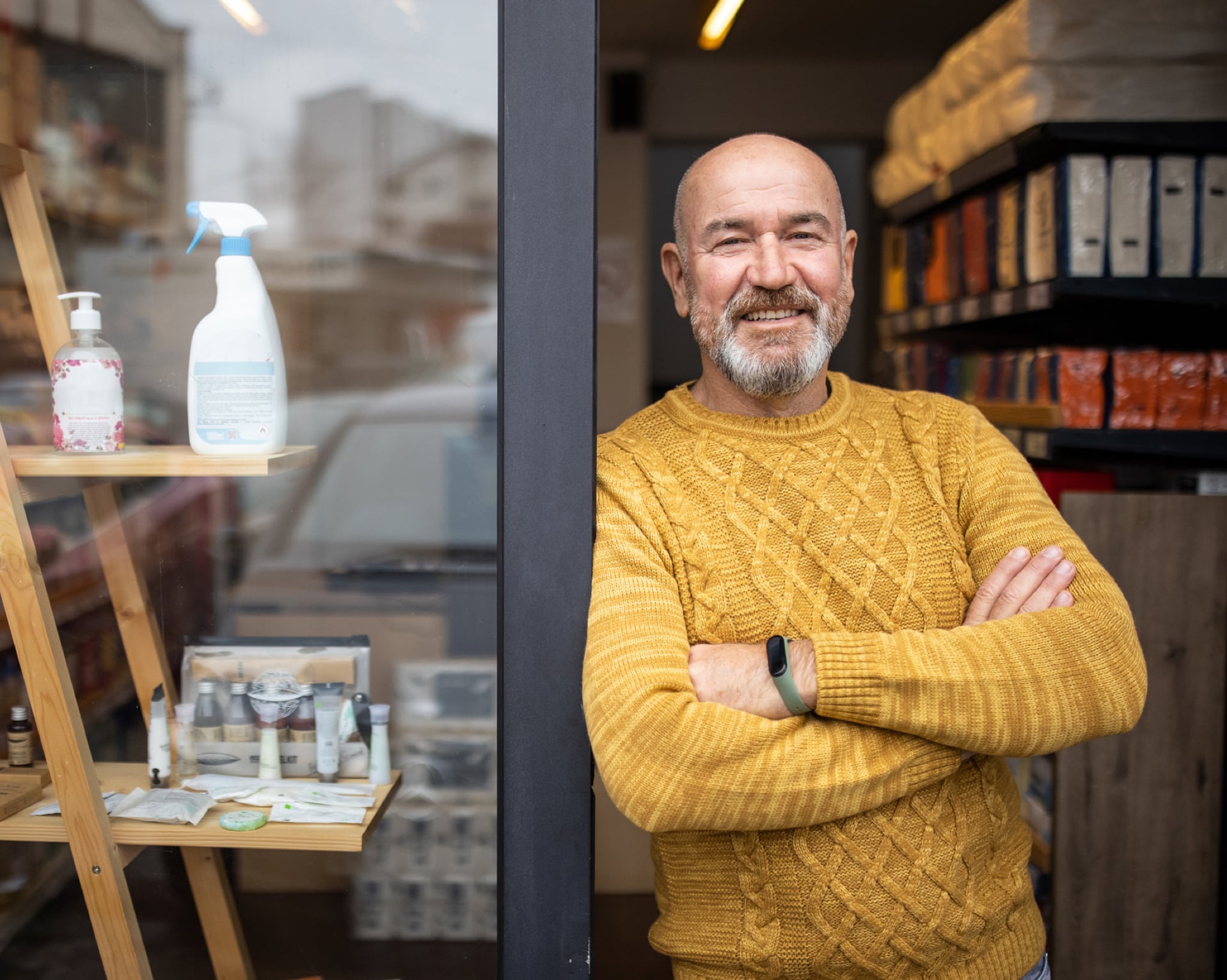A smiling man leans against a store's entryway.