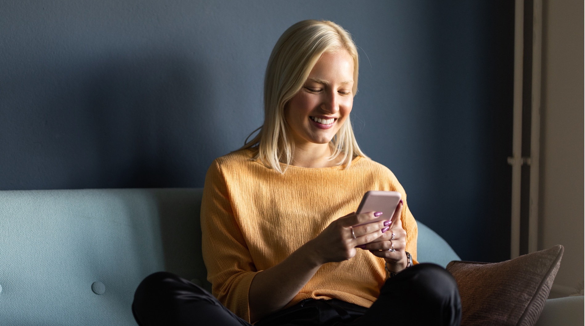 A smiling woman sitting on her couch shopping from her mobile phone.