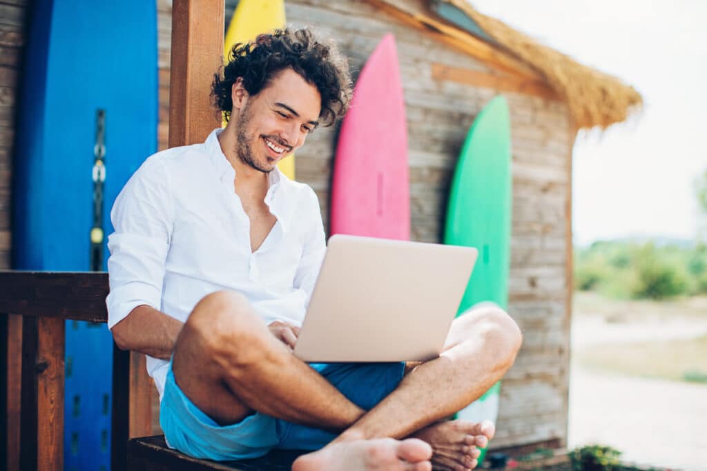 A man sits working on his laptop in front of a display of brightly coloured surfboards.